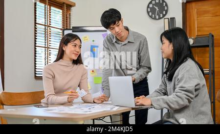 Beautiful millennial Asian female graphic designer discussing work with her team in the meeting. user experience and interface design concept Stock Photo