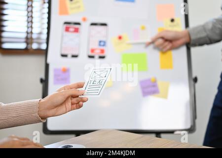 A female hand holding a mobile application interface design paper over the blurred background of the meeting. cropped and close-up image Stock Photo