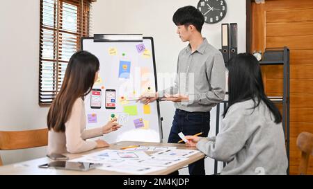 Professional young Asian male software developer presenting his information for a new mobile application to his colleagues in the meeting. Stock Photo