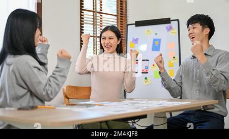 Cheerful and excited millennial Asian developers are celebrating their success together in the meeting room. teamwork, coordination, successful Stock Photo