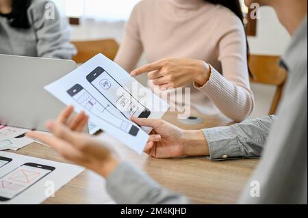 A professional male mobile app developer looking at a prototype paper, in the meeting with his team. cropped and close-up image Stock Photo