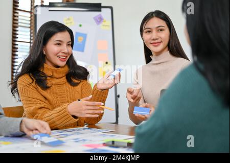 Beautiful millennial Asian female UI designer discussing and presenting her new prototype with her team in the meeting. Stock Photo