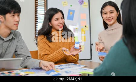 Charming and smart millennial Asian female mobile application designer presenting and sharing her ideas to her team during the meeting. UX UI concept Stock Photo