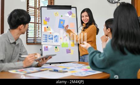Professional millennial Asian female graphic designer presenting her new prototype of her new mobile application to her team in the meeting. UX UI sta Stock Photo