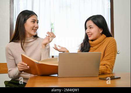 Two pretty Asian female college friends are enjoy talking and discussing their school project. tutoring, teaching, training, coaching Stock Photo