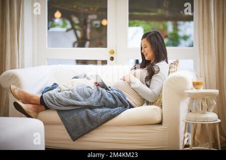 Making her maternity leave a comfortable one. a pregnant woman using a digital tablet at home. Stock Photo