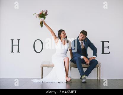 Hes all mine. Concept studio shot of a bride and groom making an M in the word home against a wall. Stock Photo