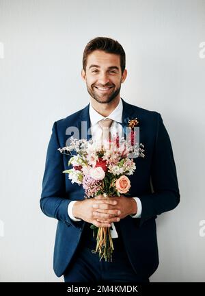 I got these for you. Studio shot of a handsome young groom holding a bunch of flowers a gray background. Stock Photo