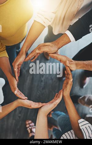 It takes a joint effort to keep success going around. High angle shot of a group of unidentifiable businesspeople forming a circle with their hands. Stock Photo