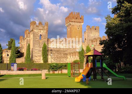 Lazise: Castle glowing gold soon after sunrise and children’s playground at Lazise on Lake (Lago) Garda, Verona, Veneto, Italy Stock Photo