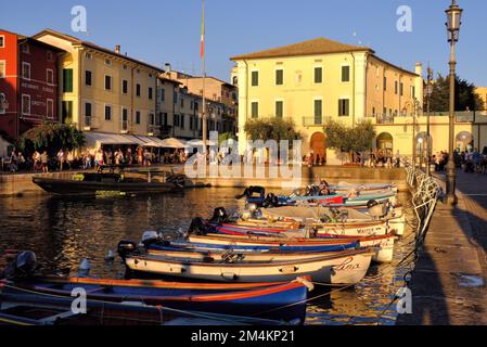 Lazise: Fishing port and marina with boats moored and restaurants glowing gold soon before sunset at Lazise on Lake (Lago) Garda, Veneto, Italy Stock Photo