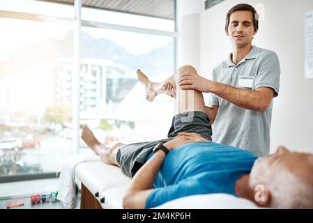 No pressure involved. a young male physiotherapist helping a client with leg exercises whos lying on a bed. Stock Photo