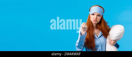 Who disturbed my sleep. Mad and displeased, angry grumpy redhead woman threaten sibling being too loud in morning, shaking fist frowning, holding Stock Photo