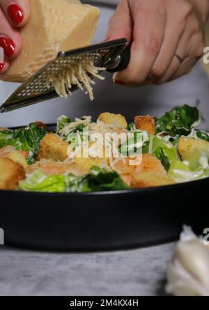 woman grating parmesan cheese on top of Caesar salad with shrimp Stock Photo