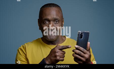 Mature man standing in studio on gray background holding mobile phone browsing social network sports athlete watching on internet physical exercise Stock Photo