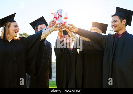 Well accomplish more great things from here on. a group of students holding their diplomas together on graduation day. Stock Photo
