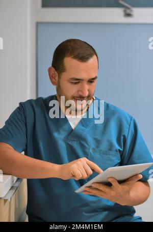 Looks like I have a full day today. a cheerful young male dentist working on his laptop while standing in his office. Stock Photo