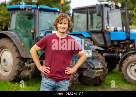 Cheerful farmer standing outside between two tractors Stock Photo