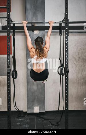 Hang on and keep going and achieve your fitness goal. Rearview shot of an unrecognizable woman doing pull ups in a gym. Stock Photo