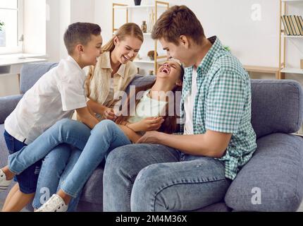 Happy family are playing together, they tickling a girl sitting on couch and laugh in living room. Stock Photo