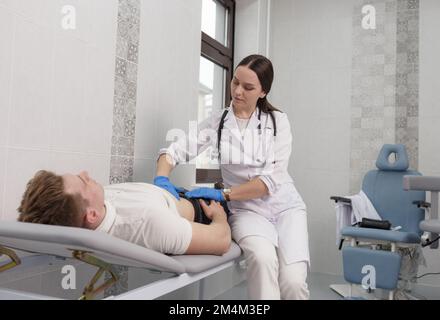 A focused young woman doctor conducting abdominal palpation in a middle-aged patient suffering from pain young man. Stock Photo