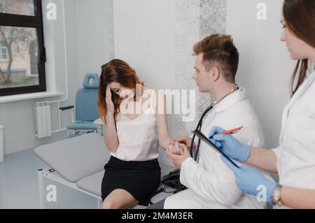 a patient in the clinic complains to the doctor about feeling unwell. the doctor measures the patient's pulse while sitting in the office Stock Photo
