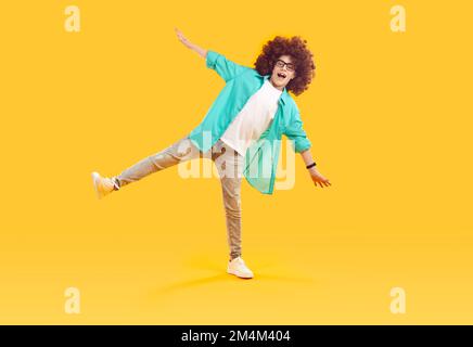 Happy, cheerful, funny boy in red curly wig, dressed in casual clothes, fooling around and dancing Stock Photo