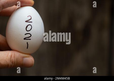 white chicken egg with the written year 2021 in a woman's hand close-up on a blurred background
