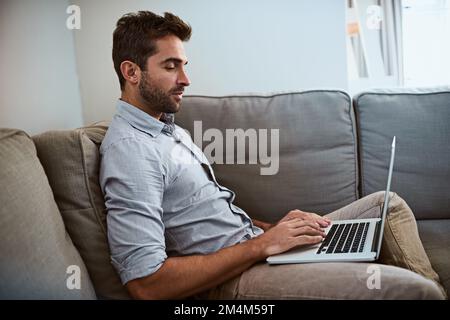Taking it easy today. a focused young man working on his laptop while being seated on a couch at home during the day. Stock Photo