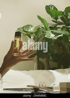 Woman is holding perfume bottle with her hand in a modern room with tree Stock Photo