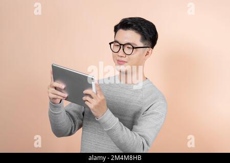 Happy attractive young man standing and using tablet over beige background Stock Photo