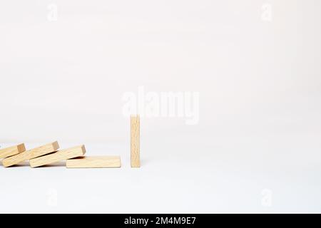 One domino stands, and other wooden dominoes fall in a row. Chain reaction, domino effect on a white background. Stock Photo