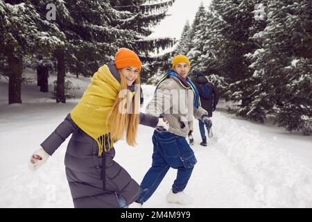 Positive excited young couple having fun running hand in hand through snowy forest. Stock Photo