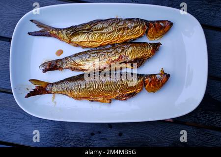 Three bucklings, freshly smoked herring, on a white serving platter, as so-called 'golden Bornholmers' a specialty on the island of Bornholm, Denmark. Stock Photo