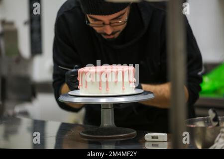 cake chef designer preparing a pink dripping on white frosted cake for baby girl birthday celebration at kitchen lab Stock Photo