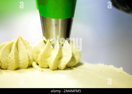 pastry chef designer making swirls with piping bag pistachio cream filling on layered green frosted chocolate cake Stock Photo