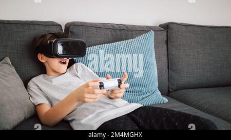 Caucasian boy enjoying at home, gaming using VR box, virtual reality goggles, and simulator, moving and physically interacting with a virtual world Stock Photo