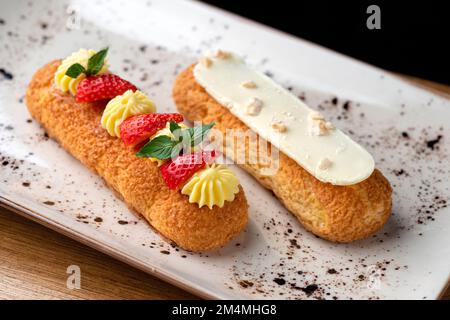 Eclair made with cream and hazelnut in plate on a wooden table. Healthy food, close up Stock Photo