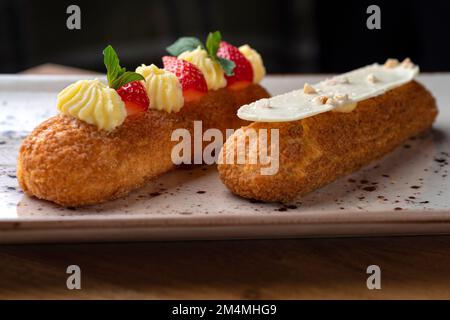 Eclair made with cream and hazelnut in plate on a wooden table. Healthy food, close up Stock Photo