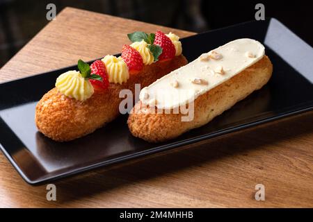 Eclair made with cream and hazelnut in plate on a wooden table. Healthy food, close up Stock Photo
