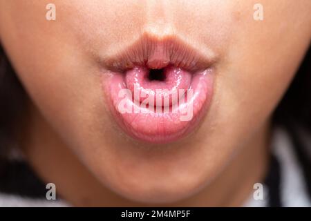 Macro of a little girl's mouth curling her tongue into a U shape, a genetic trait inherited from her parents. Stock Photo