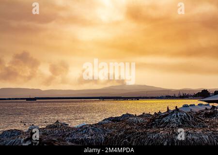Tranquil seacoast with mountains panorama and fire over horizon isolated. Orange sky cloudscape in tropical location outdoors Stock Photo