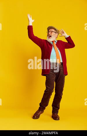 Portrait of senior man in classical clothes, glasses and cap posing over vivid yellow background. Positive emotion Stock Photo