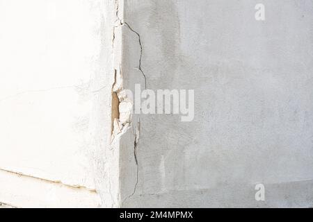 Damage in the corner of an external white moor. Showy cracks and part of the plaster fallen off. Concept of using poor materials and decay Stock Photo