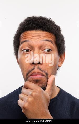 young african man with puzzled and doubtful expression with hand under chin while looking sideways. Stock Photo