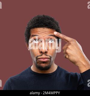 Portrait of African man pointing finger on wrinkles on the forehead, isolated on colored background. Concept of signs of age and male blemishes. Stock Photo