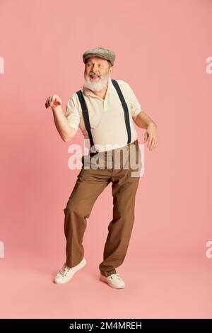 Portrait of senior man in classical clothes posing, dancing over pink background. Cheerful, good mood Stock Photo