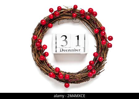 Christmas wreath decorated with red berries, wooden calendar date 31 December isolated on white background Concept of Christmas preparation, atmosphere Wishes card Hand made Christmas wreath Flat lay. Stock Photo