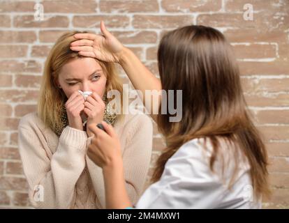 Tips how to get rid of cold. Woman feels badly ill sneezing. Girl in scarf hold tissue while doctor examine her. Recognize symptoms of cold. Remedies Stock Photo