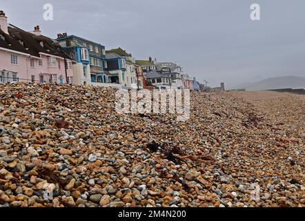 Lyme Regis, UK. 22nd Dec, 2022. On a cold damp afternoon at Lyme Regis in East Devon, the seafront shows pebbles stacked high along the front below promenade walkway with houses, shops and cafes. Picture Credit: Robert Timoney/Alamy Live News Stock Photo
